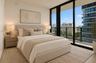 Floor-to-ceiling windows featuring urban scenery and access to an exterior balcony with a metal railing, complemented by neutral-toned interior walls 