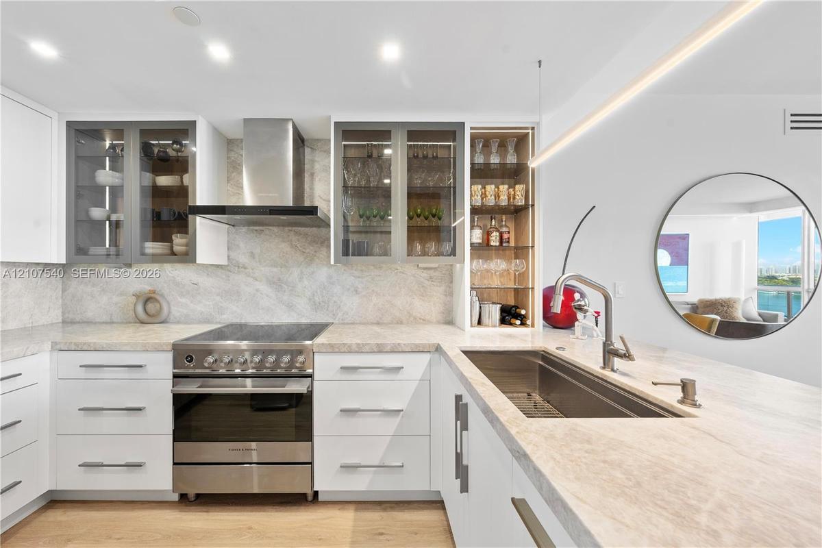 Kitchen featuring custom flat-panel cabinetry, stainless steel Fisher & Paykel gourmet stove with matching hood, built-in glass-front display shelving