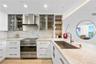 Kitchen featuring custom flat-panel cabinetry, stainless steel Fisher & Paykel gourmet stove with matching hood, built-in glass-front display shelving