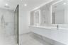 Floating double vanity with dual rectangular sinks, floor-to-ceiling stone-finish tile wall, glass-enclosed walk-in shower with rainfall fixture, and 