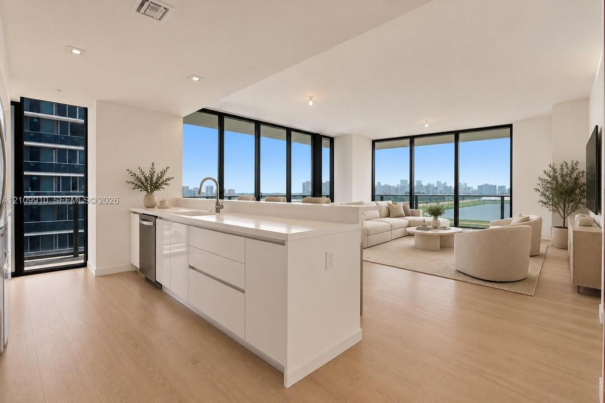 Kitchen featuring white flat-panel cabinetry, light-toned stone countertops, and stainless steel dishwasher, complemented by floor-to-ceiling windows 
