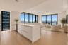 Kitchen featuring white flat-panel cabinetry, light-toned stone countertops, and stainless steel dishwasher, complemented by floor-to-ceiling windows 