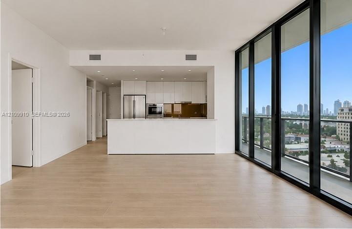 Open-concept interior featuring floor-to-ceiling glass panel walls, wood-finish flooring, white flat-panel cabinetry, stainless steel appliances, and 