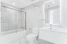Bathroom featuring large-format porcelain tile, wall-mounted floating vanity, glass tub enclosure, and backlit vanity mirror