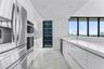 Contemporary kitchen featuring high-gloss cabinetry, stone-finish flooring, quartz countertops, stainless steel appliances, and floor-to-ceiling windo