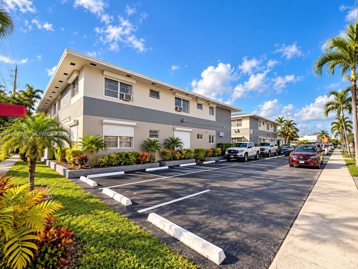 Multi-unit exterior featuring two-story modern architecture, exterior neutral-toned stucco siding, dedicated asphalt parking area, and landscaped grou
