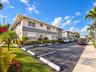 Multi-unit exterior featuring two-story modern architecture, exterior neutral-toned stucco siding, dedicated asphalt parking area, and landscaped grou