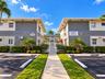 Multi-unit exterior featuring gray stone-veneer accents, paved parking area, gated pedestrian entrance, and manicured landscaping
