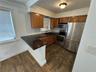 Kitchen featuring wood cabinetry, stone-surface countertops, stainless steel appliances, and multi-format tile flooring