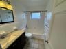 Bathroom featuring a vanity with a stone-composite countertop, white tile tub surround, ceramic tile flooring, and a framed wall mirror