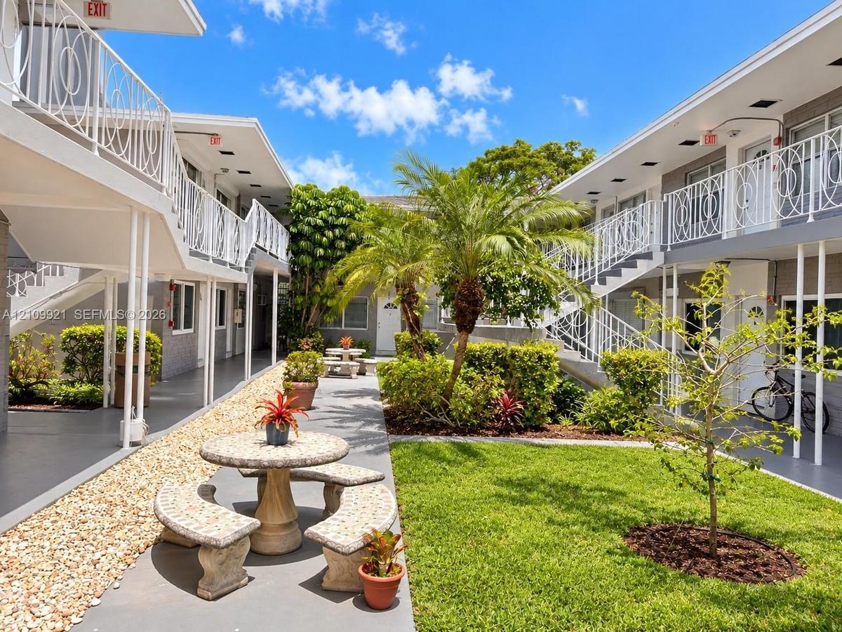Courtyard featuring a manicured lawn, stone-surfaced exterior walkways, mature palm trees, decorative white metal railings, and integrated stone seati