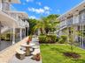 Courtyard featuring a manicured lawn, stone-surfaced exterior walkways, mature palm trees, decorative white metal railings, and integrated stone seati