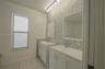 Dual white vanities with integrated rectangular basins, honeycomb-pattern mosaic tile backsplash, framed wall mirrors, and multi-bulb vanity lighting