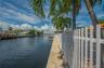 Waterfront property featuring a concrete seawall, white picket fencing, and mature palm trees