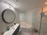 Modern floating vanity featuring an integrated basin, circular backlit mirror, glass-enclosed shower, and built-in jetted tub with tiled surround