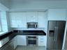 Contemporary kitchen featuring high-gloss white cabinetry, dark stone countertops, stainless steel appliances, and large-format tile flooring