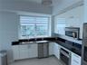 Kitchen featuring high-gloss white cabinetry, dark stone-finish countertops, stainless steel appliances, large double-basin under-mount sink, and a mo