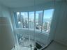 Double-height floor-to-ceiling windows featuring city and water scenery, glass partition railing, and private balcony with wood-finish flooring