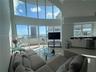 Double-height floor-to-ceiling windows, polished tile flooring, glass balcony enclosure, and wet bar featuring white cabinetry with a dark countertop