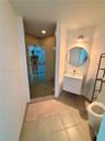 Bathroom featuring a glass-enclosed shower with tiled surround, wall-mounted white vanity with a rectangular sink, circular mirror, and large-format f