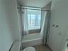 Bathroom featuring a built-in bathtub, light-toned ceramic tile surround, integrated shower fixture, and a large window with an expansive urban skylin