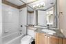 Bathroom featuring a vanity with stone-finish countertop, undermount sink, large mirror with mosaic tile trim, white tile shower surround, and contemp