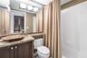 Bathroom vanity featuring stone-finish countertop, geometric vessel sink, dark wood-tone cabinetry, tiled tub surround, and framed mirror with mosaic 
