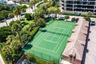 Tennis court featuring a perimeter fence, surrounding mature landscaping, palm trees, and an attached structure with a terracotta-style tile roof
