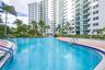 Swimming pool featuring a concrete deck with perimeter landscaping, metal handrails, and surrounding high-rise residential structure with private balc