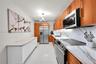 Galley kitchen featuring wood cabinetry, stone-surface countertops with matching backsplashes, stainless steel appliances, polished tile flooring, and