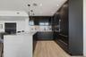 Contemporary kitchen featuring custom dark cabinetry, stone-surfaced waterfall island, integrated built-in appliances, recessed lighting, and wood-fin