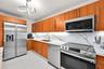 Kitchen featuring wood-finish cabinetry, stone-patterned backsplash, stainless steel appliances, under-cabinet lighting, and large-format tile floorin