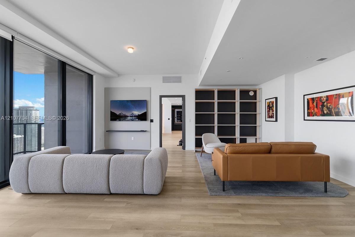 Open-concept living space featuring wood-finish flooring, floor-to-ceiling glass sliding doors, built-in floor-to-ceiling shelving, and a wall-mounted