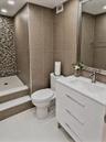 Bathroom featuring a modern white vanity, glass-tiled shower wall accent, large-format neutral wall tiling, stepped shower entry, and a framed mirror