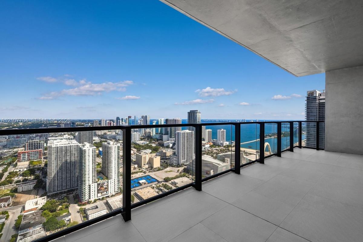 Covered balcony with large-format tile flooring and sleek black metal railing featuring transparent glass panels