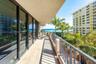 Covered balcony featuring tile flooring, full-height sliding glass doors, and metal railings with water and palm tree scenery