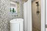 Bathroom featuring a pedestal sink, wall-mounted faucet, mosaic tile backsplash, walk-in shower with stone tile walls, and handheld shower fixture