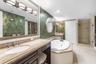 Bathroom featuring a stone-topped vanity with undermount sink, jetted soaking tub, glass-enclosed shower, decorative wall coverings, and integrated li