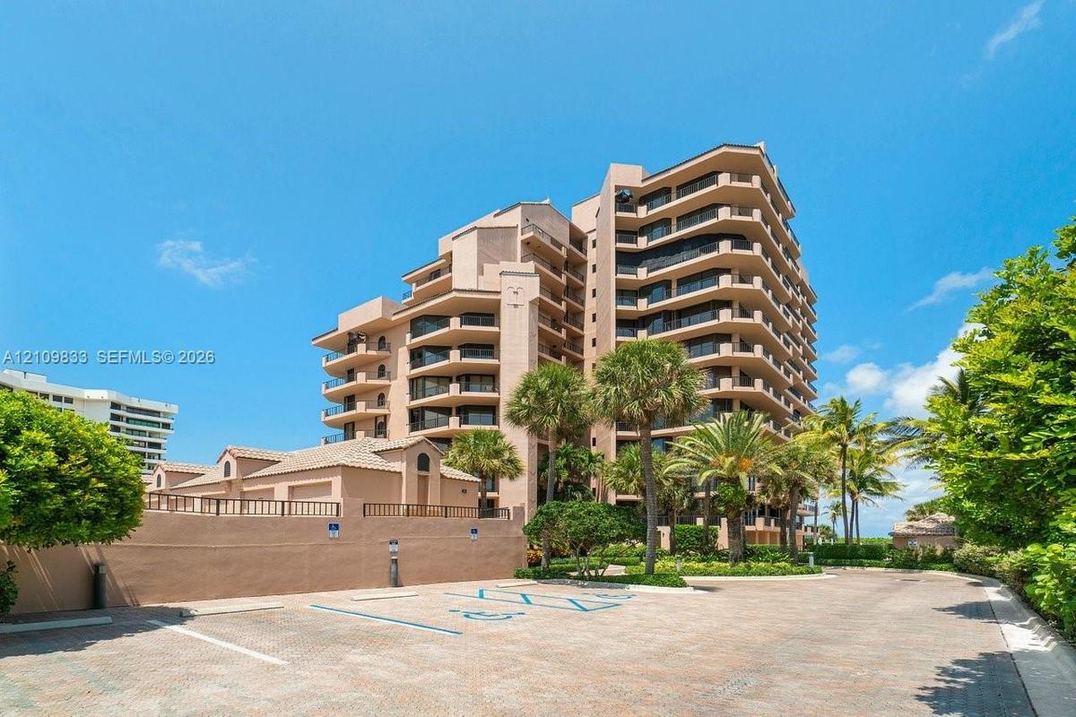 Multi-story high-rise building featuring private balconies, masonry exterior, paved parking area, and mature palm trees