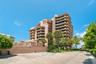Multi-story high-rise building featuring private balconies, masonry exterior, paved parking area, and mature palm trees