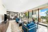 Living area featuring floor-to-ceiling windows, full-wall custom dark wood built-in cabinetry with integrated desk space, and neutral stone-finish flo
