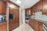 Kitchen featuring dark wood cabinetry, panel-front refrigerator, stainless steel built-in double ovens, multi-colored glass tile backsplash, and stone