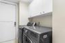 Laundry area featuring white built-in upper cabinetry with polished metal hardware and a solid-core entry door with a deadbolt lock