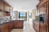 Kitchen featuring custom wood cabinetry, mosaic tile backsplash, stone countertops, recessed lighting, and tile flooring