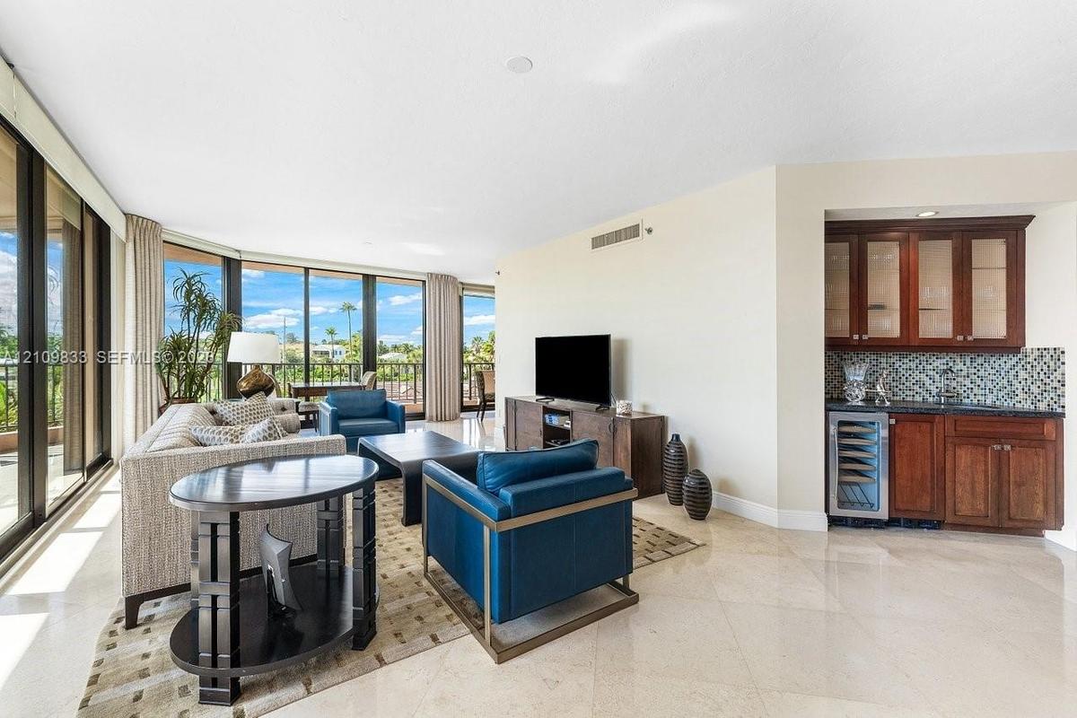 Floor-to-ceiling windows, polished stone flooring, and a built-in wet bar featuring dark wood cabinetry, glass-front upper cabinets, a mosaic tile bac
