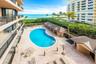 Community pool area featuring a kidney-shaped swimming pool, paver deck, covered cabanas with tiled roofs, and direct oceanfront presence