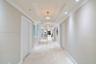 Grand gallery hallway featuring stone tile flooring, multi-tiered tray ceilings, recessed lighting, and decorative semi-flush mount fixtures