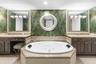 Dual vanities with stone countertops, jetted soaking tub, decorative wall covering, and two framed wall mirrors