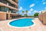 Swimming pool with a curved concrete deck, metal handrail, perimeter privacy fencing, and exterior balconies