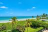 Coastal property featuring direct ocean frontage, manicured landscaping with mature palms, and an outdoor swimming pool